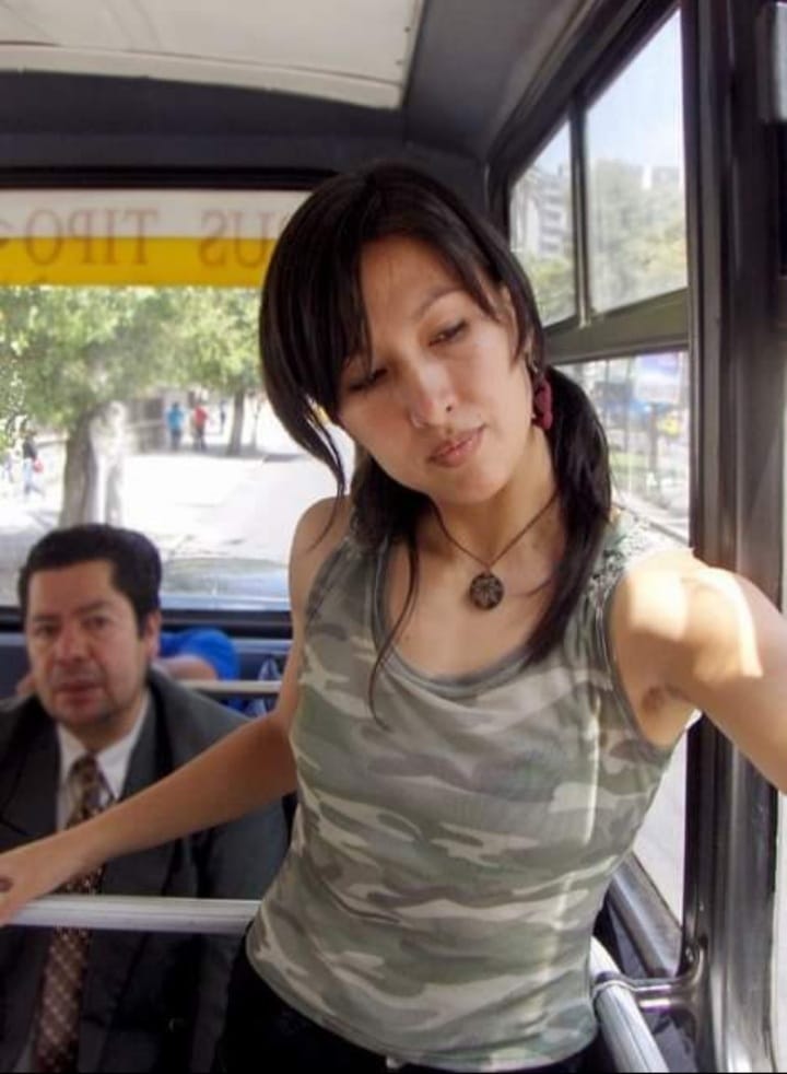 En un bus urbano. Una mujer de pie ubicada en el espacio de uso de sillas de ruedas.