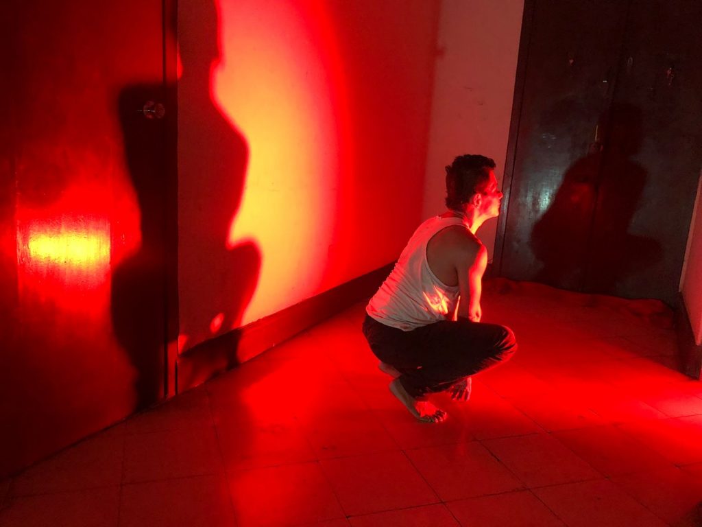 Jorge Parra en un escenario mientras le ilumina una luz. Sentado en cuclillas, mira hacia un lado.